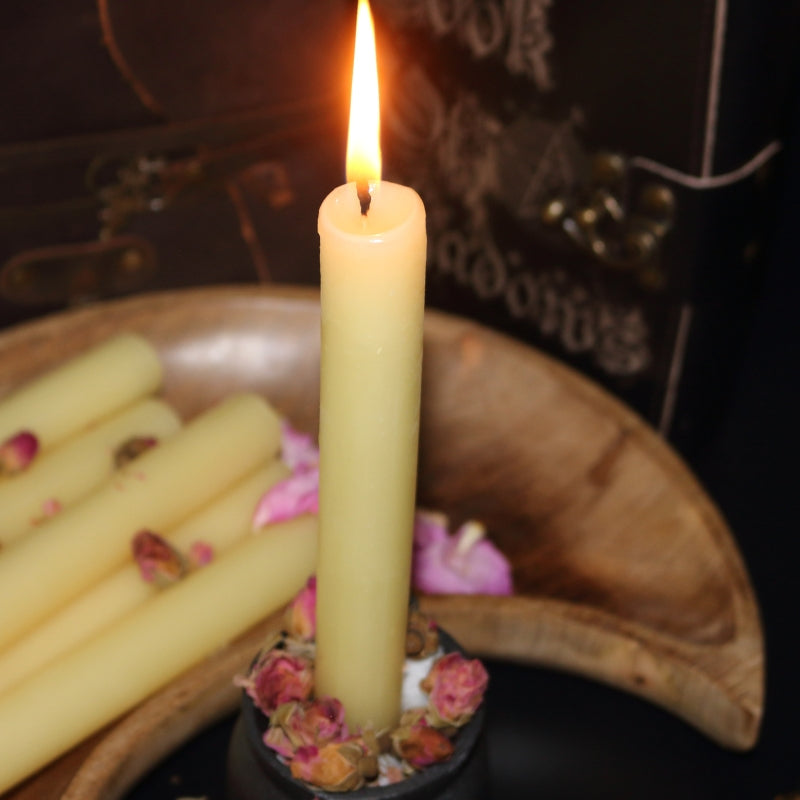 lit beeswax candle sitting in a cauldron, in front of a wooden crescent moon shaped bowl with a brass embellished candle snuffer and old leather journals