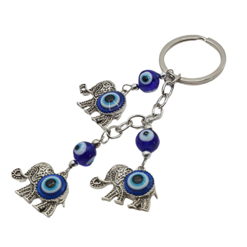 3 silver elephants with a blue and white evil eye bead in the centre of them, attached to a silver chain and ring on a white background