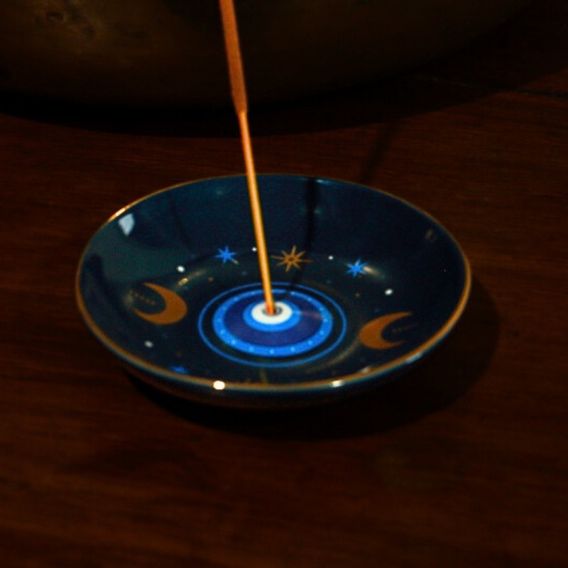 Incense stick on a decorative plate with evil eye design on a dark surface
