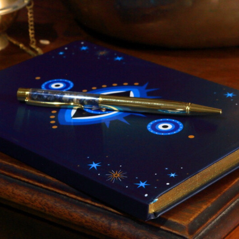 Blue notebook with star and evil eye designs on a wooden surface, accompanied by a pen.