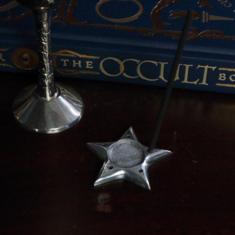 Aluminium Star Incense Holder with an incense stick, in front of "The Occult Book" and silver chalice
