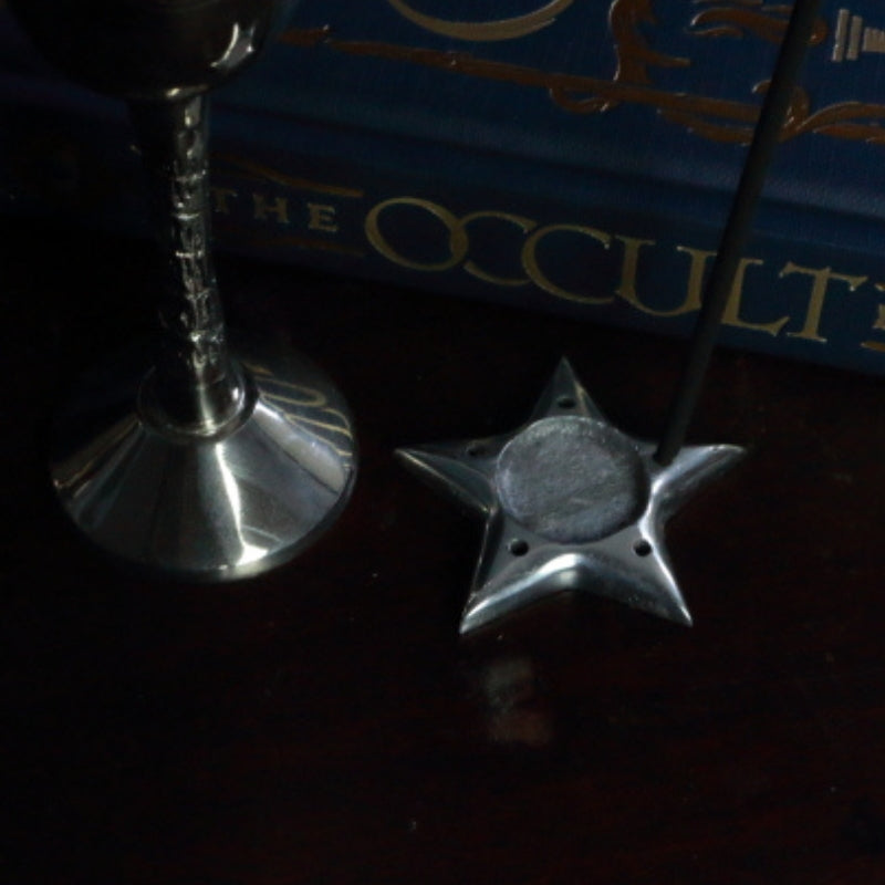 Aluminium Star Incense Holder with an incense stick in front of "The Occult Book" and silver chalice
