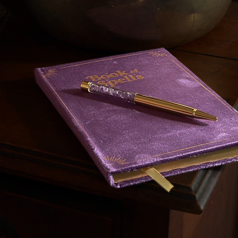 Purple Book of spells journal with amethyst chip gold pen on wooden table