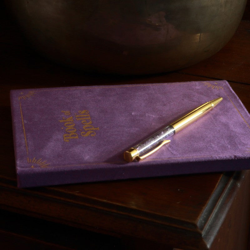 Purple Book of spells journal with amethyst chip gold pen on wooden table