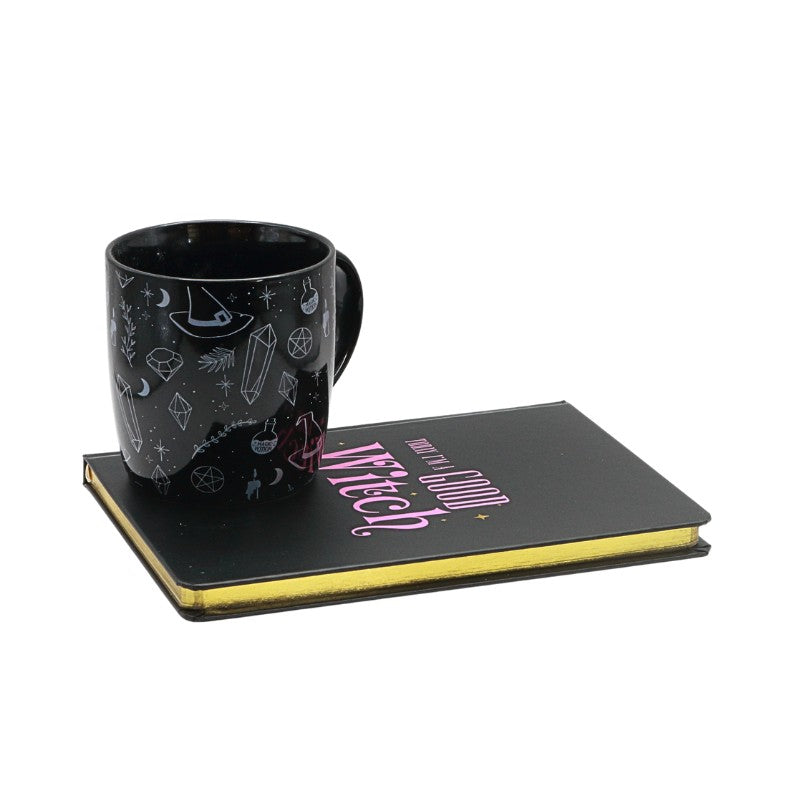 Black mug with decorative patterns on a black journal with 'today im a good Witch' text, on a white background