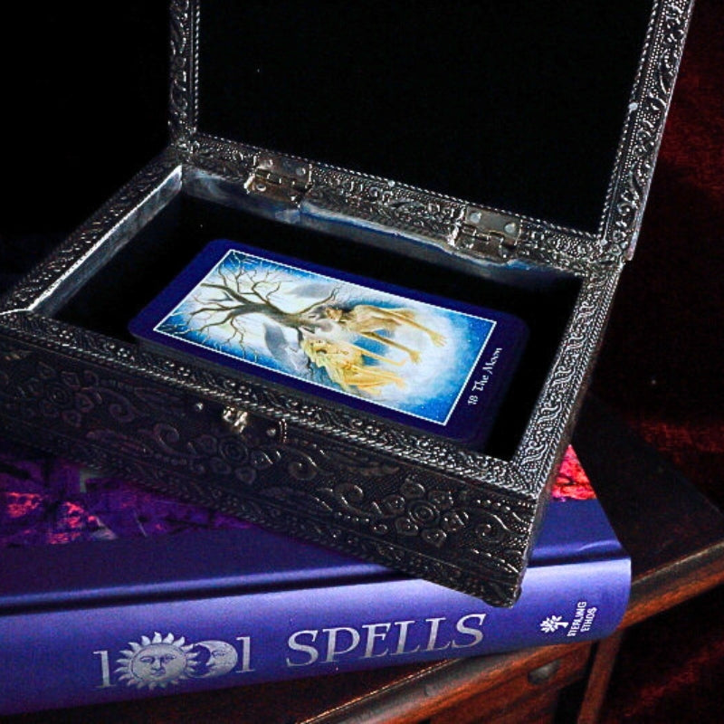 Embossed Metal Tarot Box open with shapeshifter tarot cards inside, on top of a book of spells