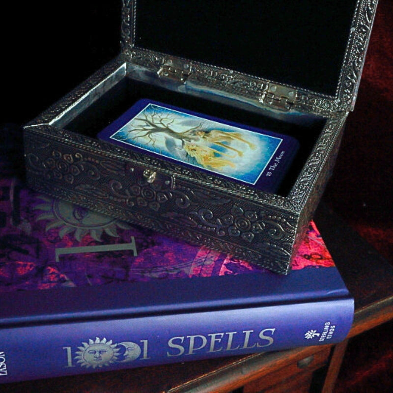 Embossed Metal Tarot Box open with shapeshifter tarot cards inside, on top of a book of spells