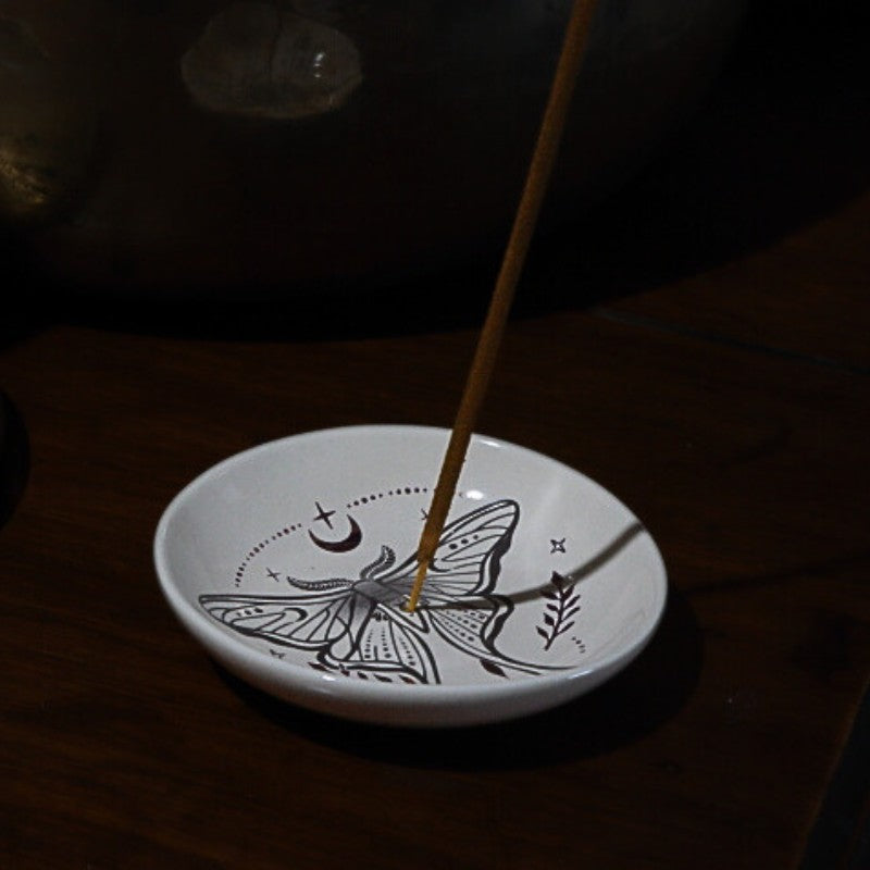 Incense stick on a white ceramic dish with black designs in a dark setting