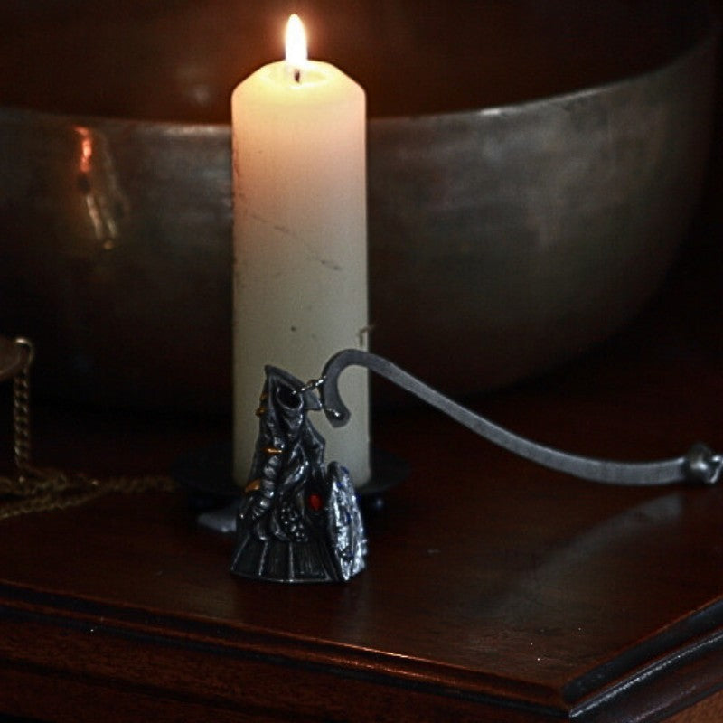 dragon head candle snuffer in front of a beeswax candle on a wooden table