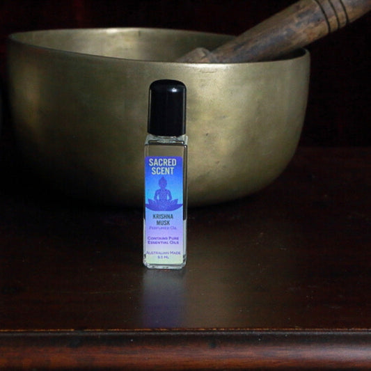 Bottle of Sacred Scents Perfume Oil sitting on a wooden apothecary cabinet in front of a brass singing bowl