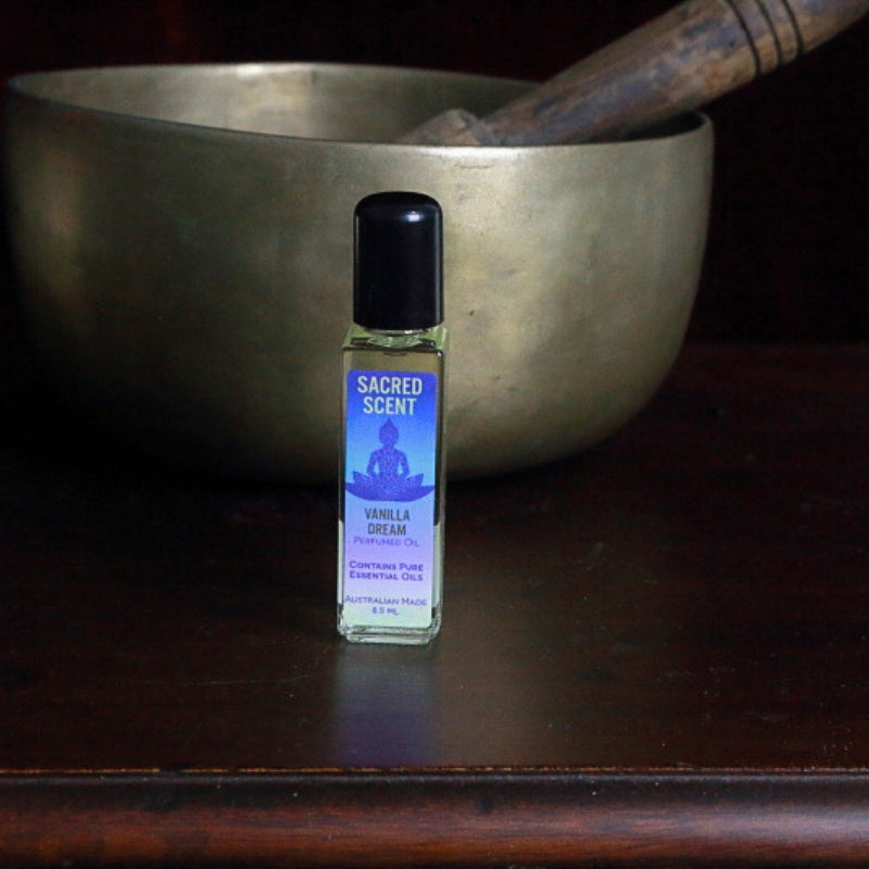 Bottle of Sacred Scents Perfume Oil sitting on a wooden apothecary cabinet in front of a brass singing bowl