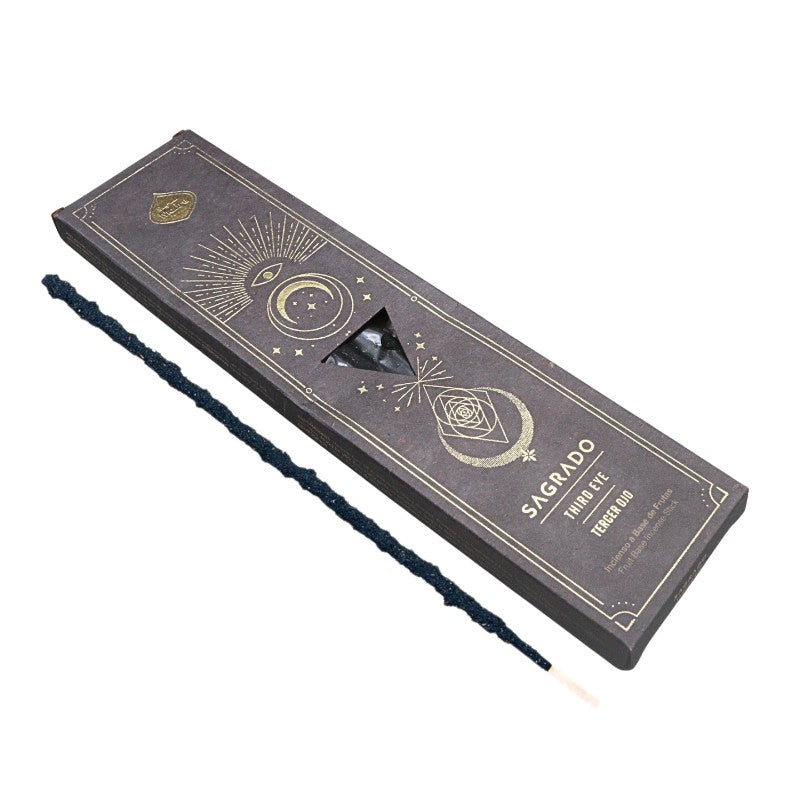 A dark charcoal gray box of Sagrado Triple Eye Tempo Zap incense sticks, shown with one unlit dark blue-black twisted incense stick placed diagonally in front of the box on a plain white background.