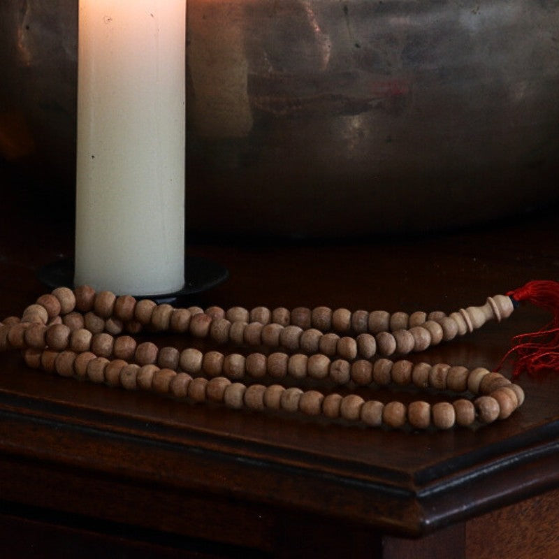 Sandalwood Beaded  Japa mala Prayer Beads on wooden table in front of singing bowl and beeswax candle