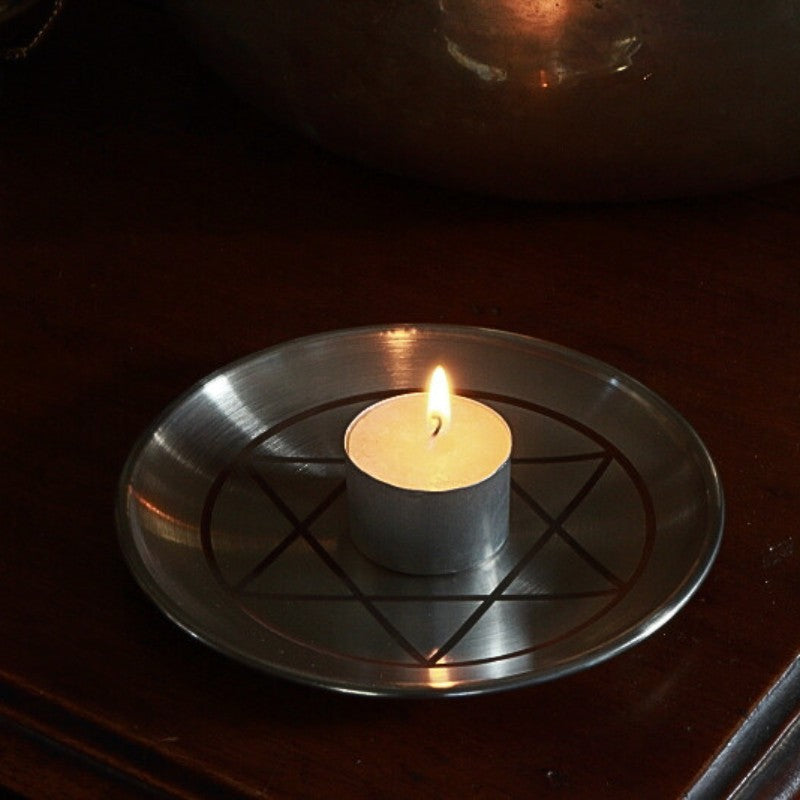 Candle on a metal tray with solomon's seal design on a dark surface