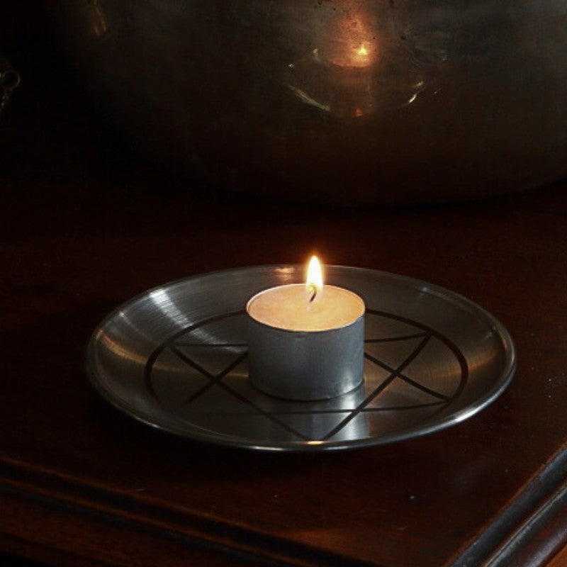 tealight candle on a metal tray with solomon's seal design on a dark surface