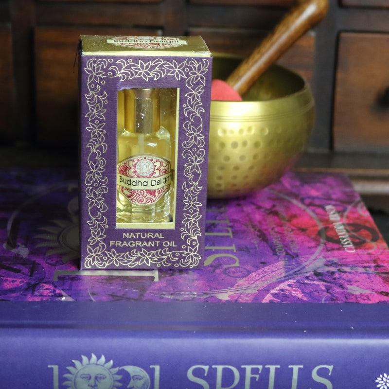 purple and gold box containing a miniature perfume bottle, sitting on a purple and pink book of spells in front of a brass singing bowl with wooden striker. in the background there is an apothecary cabinet