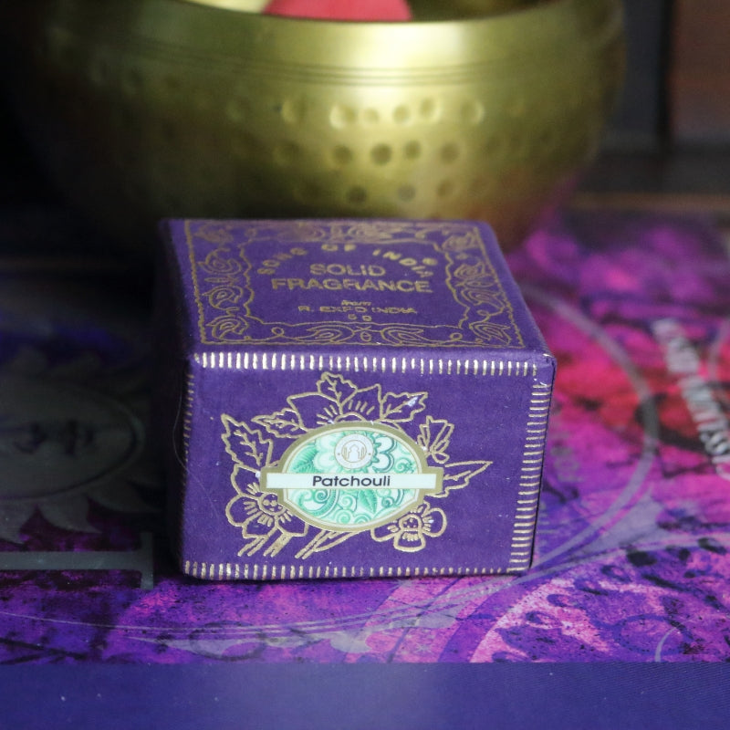 purple and gold box , sitting on a purple and pink book of spells in front of a brass singing bowl with wooden striker.