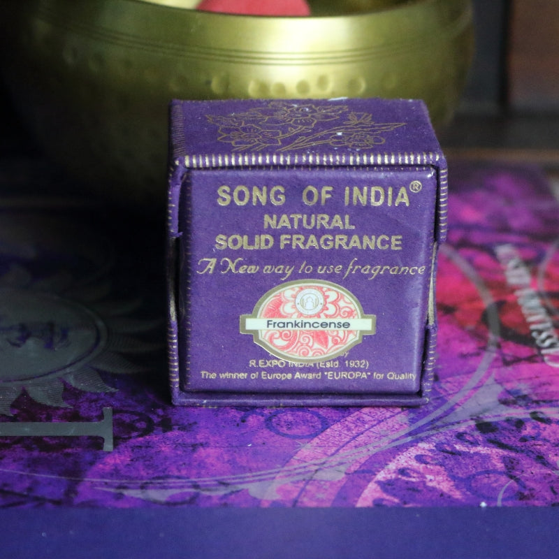 purple and gold box , sitting on a purple and pink book of spells in front of a brass singing bowl with wooden striker.