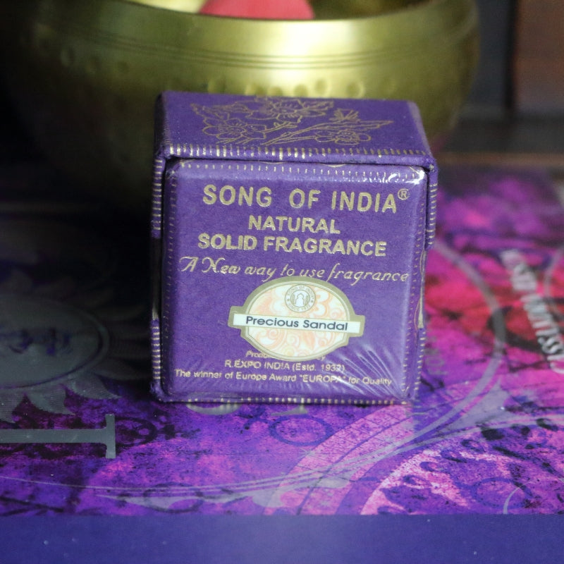 purple and gold box sitting on a purple and pink book of spells in front of a brass singing bowl with wooden striker.
