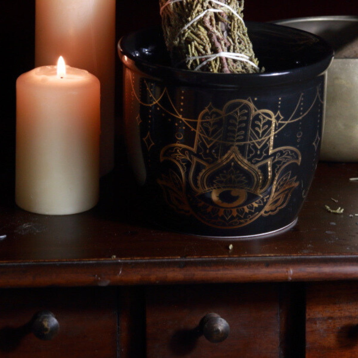 Hamsa smudge bowl next to beeswax candles with a juniper smudge stick