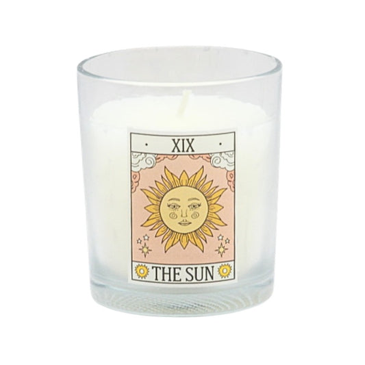Candle in a glass holder with a tarot card design featuring 'The Sun' card on a white background.