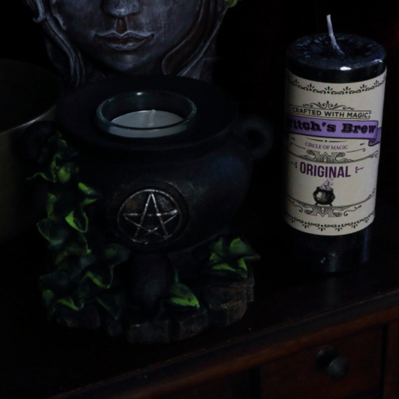 Witch's Brew original Pillar Candle next to cauldron candle holder, lady head planter and brass singing bowl