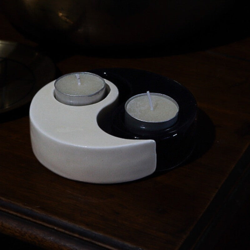 Yin and yang candle holder with two candles on a dark surface