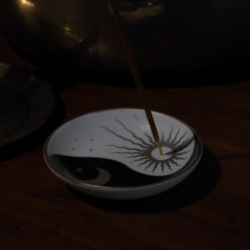Incense stick in a dish with yin and yang design on a dark background