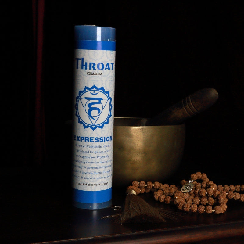 Blue throat chakra pillar candle in front of a singing bowl with mala beads