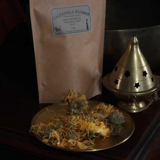 Dried calendula flowers on a gold plate with a bag labeled 'Calendula Flowers' and a brass incense burner.