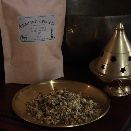 Chamomile flower package, bowl of chamomile flowers, and brass incense burner on a dark surface.