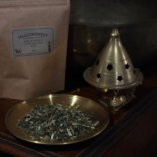 Incense cone holder and a bag labeled 'Meadowsweet' on a wooden surface.