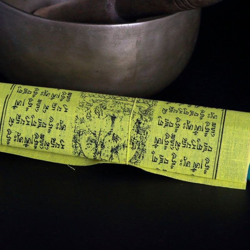 roll of tibetan prayer flags in front of a brass singing bowl