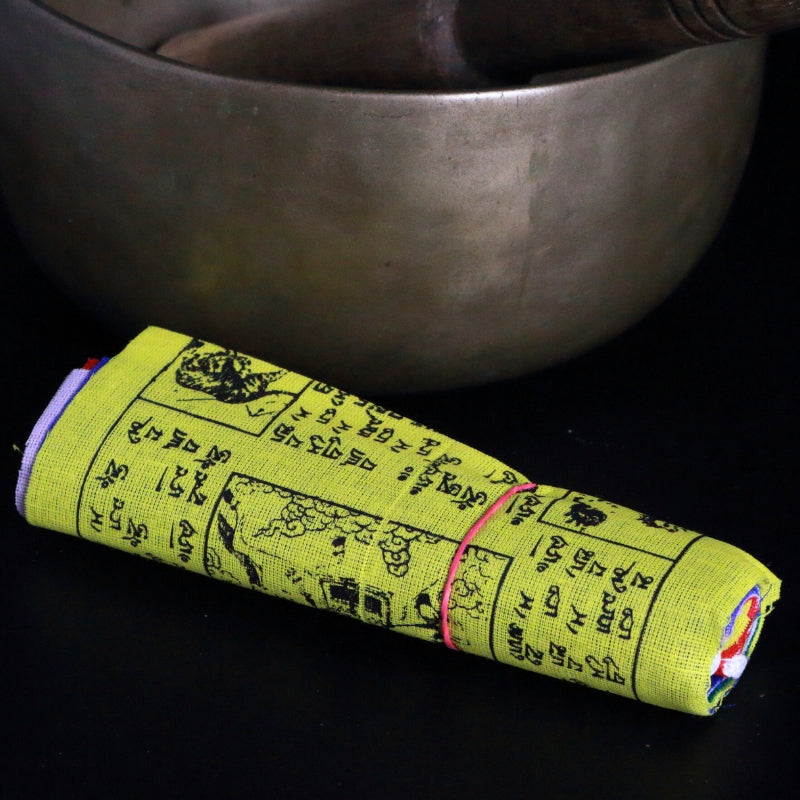 roll of tibetan prayer flags in front of a brass singing bowl