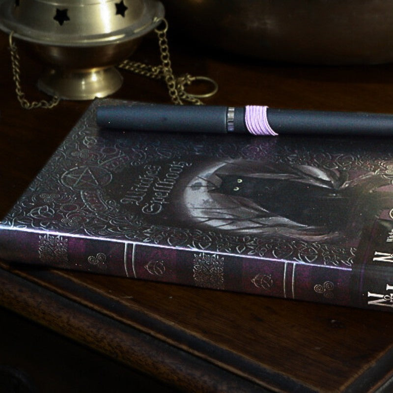 Decorative book with a black cat illustration on a wooden surface, accompanied by a pen.