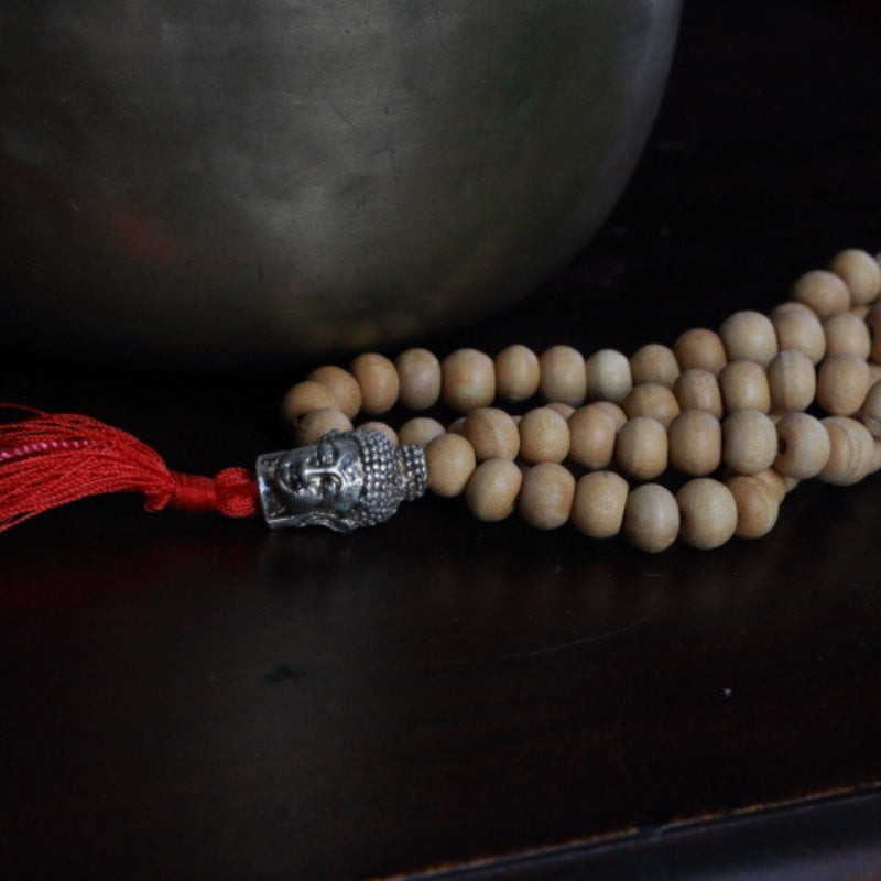 Buddha Head Natural Japa Mala Prayer Beads in front of a singing bowl, on a wooden apothecary cabinet