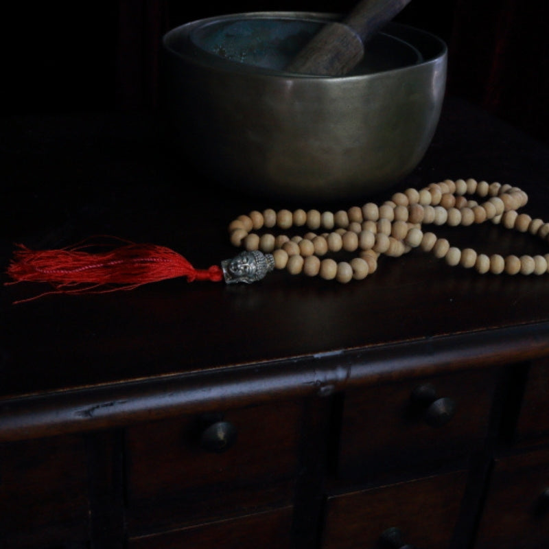 Buddha Head Natural Japa Mala Prayer Beads in front of a singing bowl, on a wooden apothecary cabinet