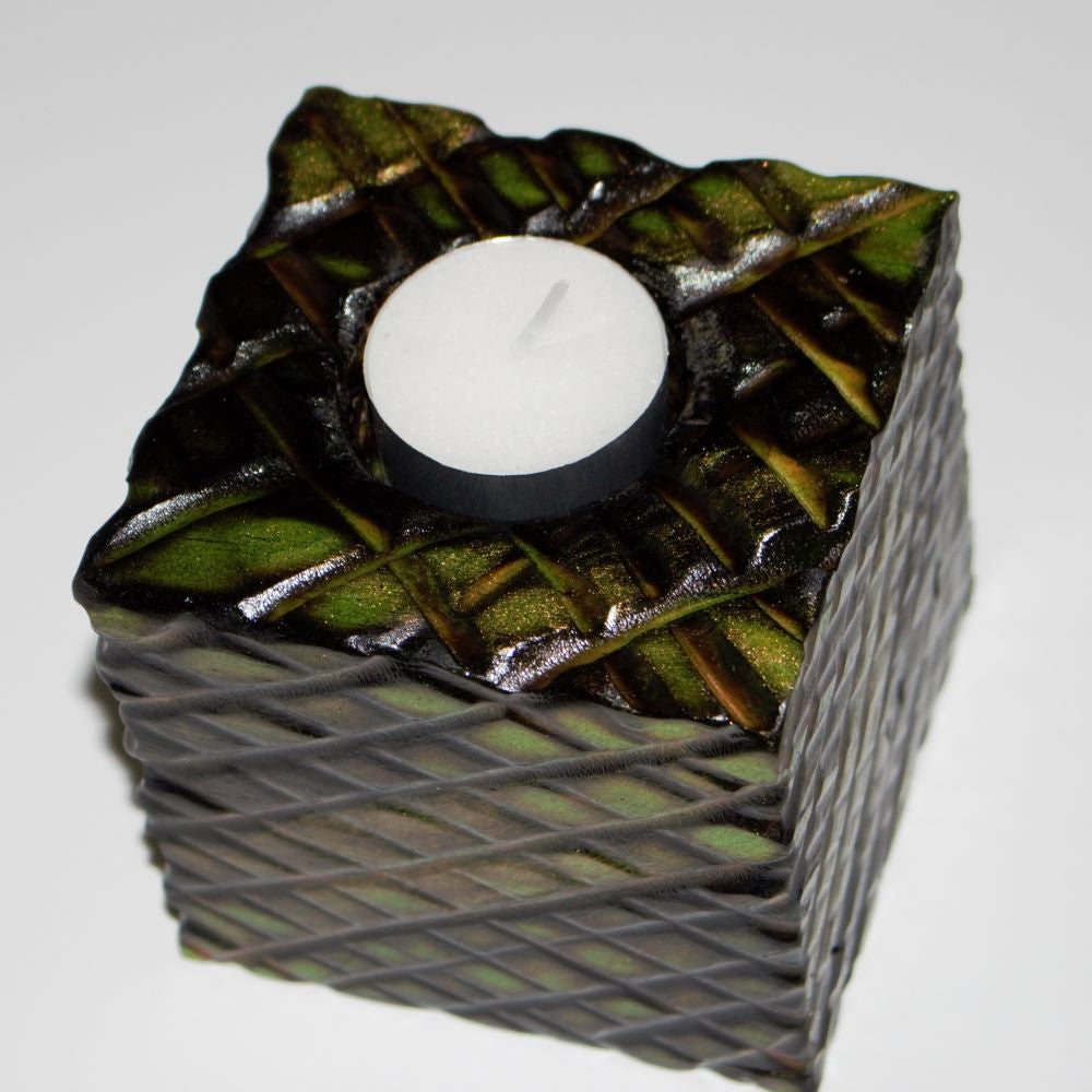 green and gold wooden square candle holder with diagonal lines etched to resemble dragon scales. Containing a white tea light candle, on a white background