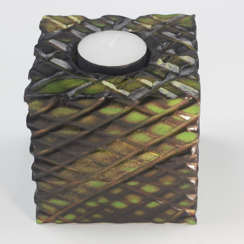 green and gold wooden square candle holder with diagonal lines etched to resemble dragon scales. Containing a white tea light candle, on a white background