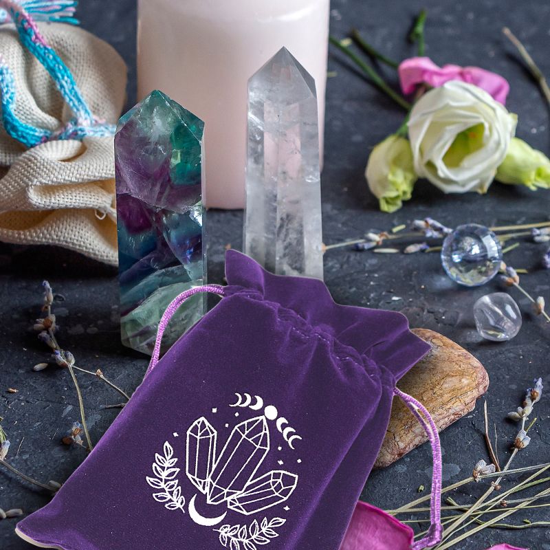 purple tarot bag with white moon and crystal print on a table with lavender sprigs, fluorite and quartz crystal single terminated crystal