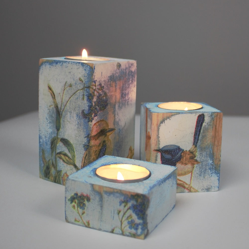 blue and white distressed set of 3 candle holders with lit tea light candles, decorated with a kookaburra, fairy wrens and blue flowers