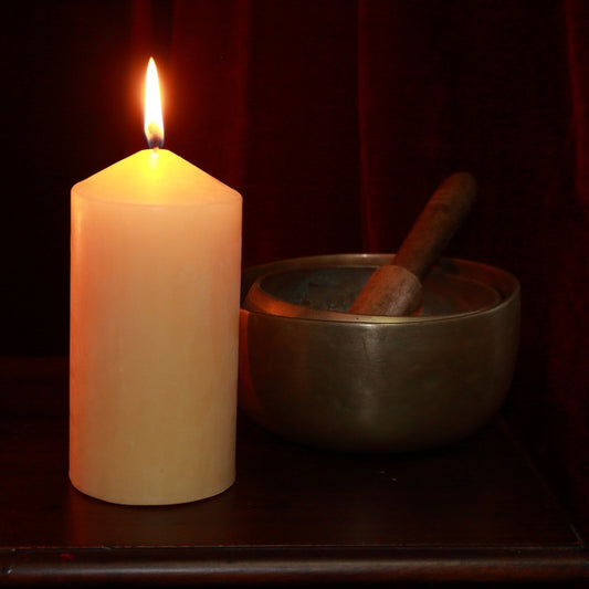 Beeswax pillar candle next to brass singing bowls