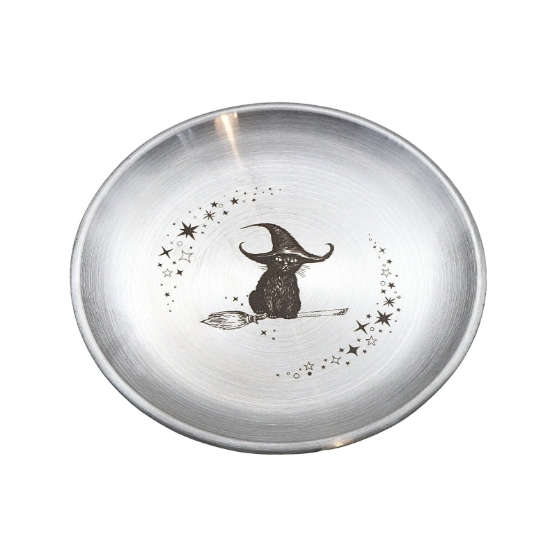 A round brushed silver metal bowl featuring a black illustration of a witch sitting on a broomstick, surrounded by small stars, on a plain white background.