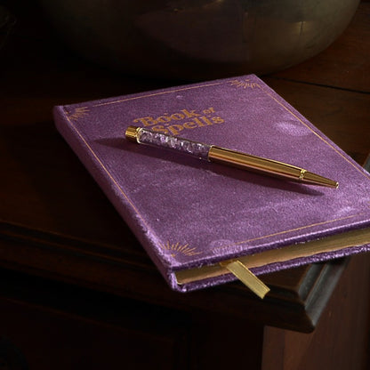 Purple Book of spells journal with amethyst chip gold pen on wooden table