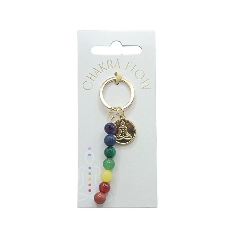 Gold keyring with rainbow coloured beads and a symbol of a person sitting in lotus pose on a white swing tag with the words "chakra flow"
