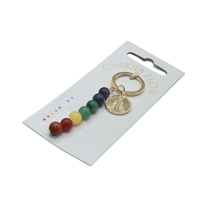 Gold keyring with rainbow coloured beads and a symbol of a person sitting in lotus pose on a white swing tag