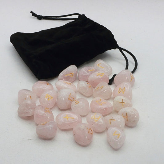 Set of pink crystal runes with gold symbols on a white surface, accompanied by a black drawstring bag.