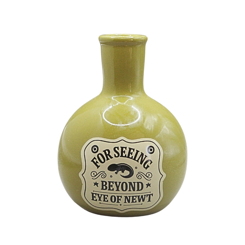 A small round ceramic vase with a short neck, in a glossy olive green glaze, featuring a vintage-style cream label with the text 'FOR SEEING BEYOND EYE OF NEWT' and a black newt illustration.
