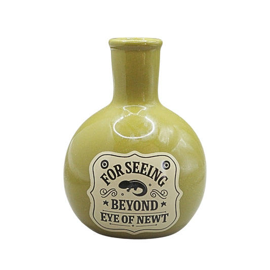 A small round ceramic vase with a short neck, in a glossy olive green glaze, featuring a vintage-style cream label with the text 'FOR SEEING BEYOND EYE OF NEWT' and a black newt illustration.