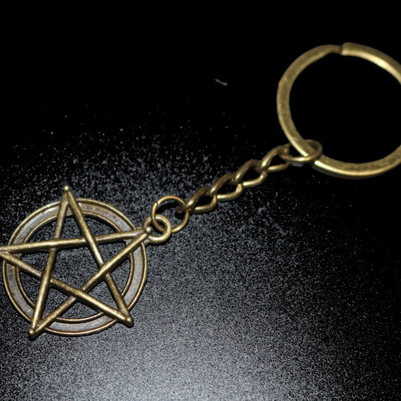 dark gold coloured key ring with a pentacle (5 pointed star within a circle) joined to a dark gold ring by a dark gold chain